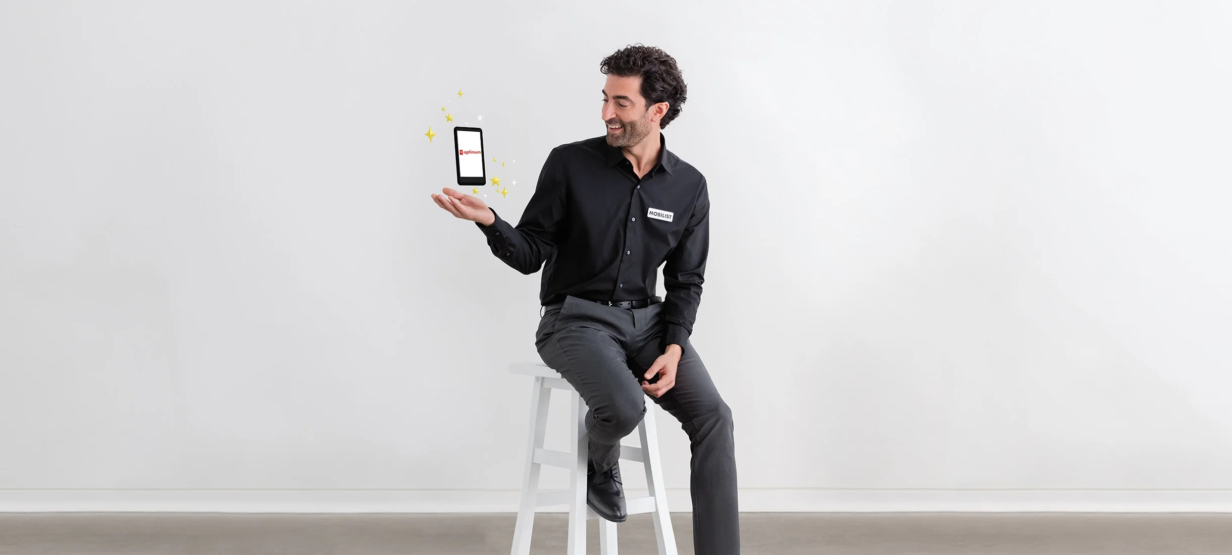 PC Optimum shows on the phone hovering over the hand of a Mobilist man perching on a white chair